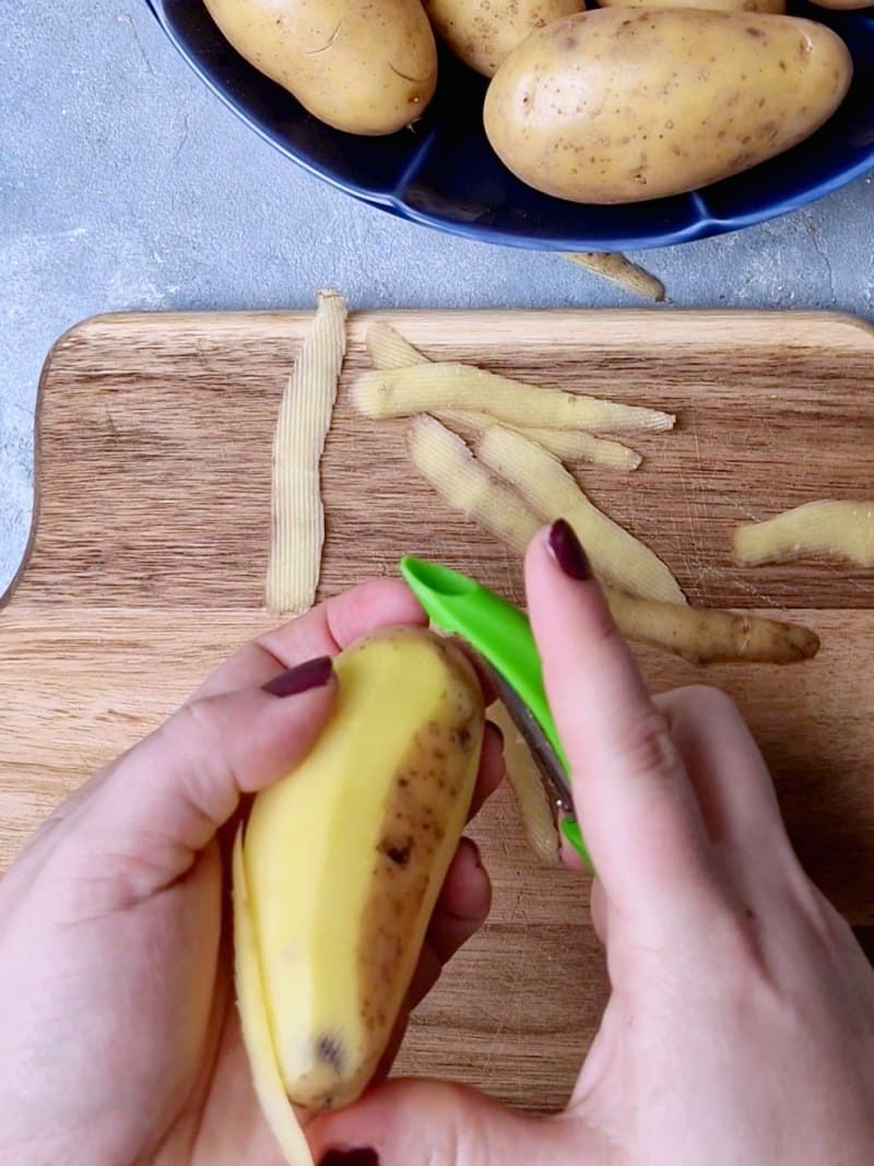 Hands peeling a large potato with a green peeler. 