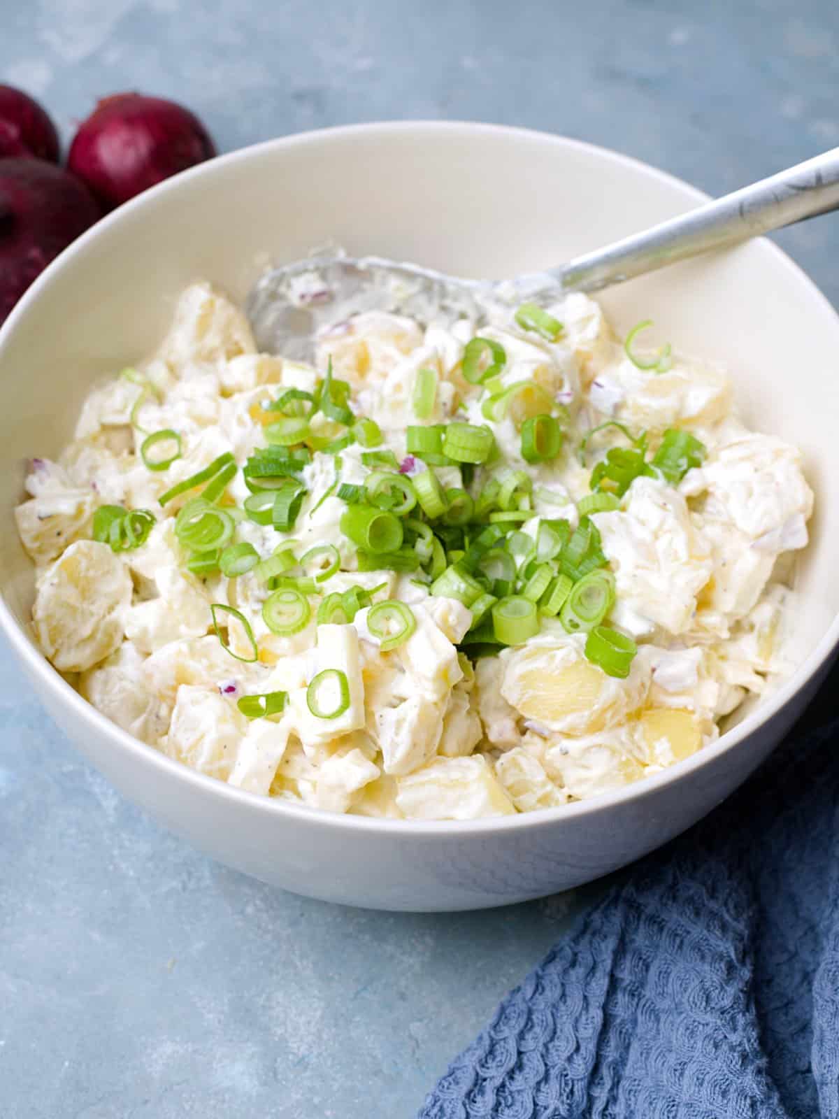 Closeup on creamy potato salad with red onion and spring onion on top.