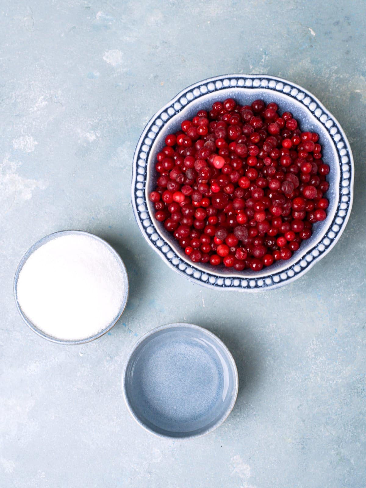 Ingredients for lingonberry jam on blue surface. 