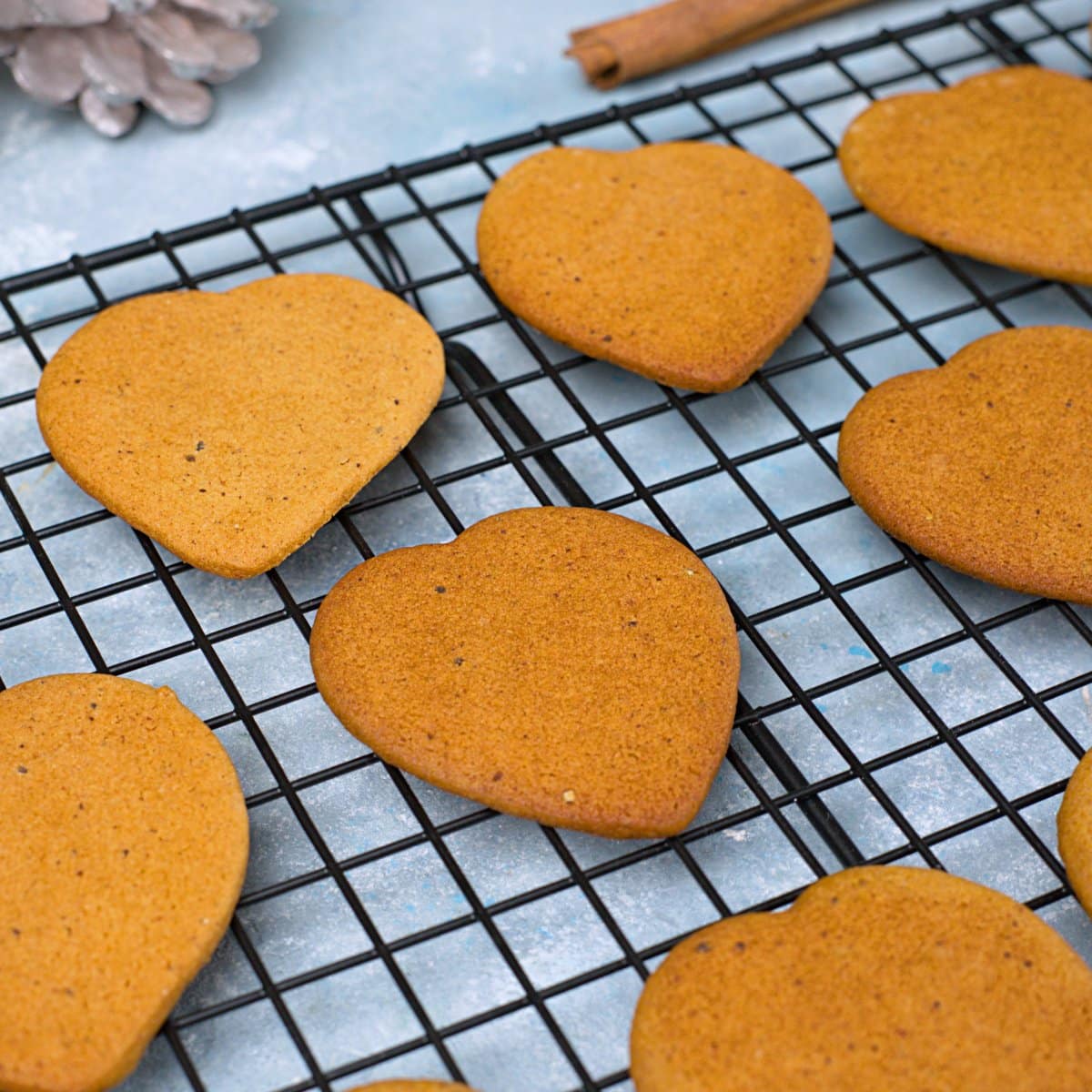 Brown thin gingerbread heart shaped cookies cooling on black rack.