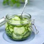 Thinly slices cucumber slices in a glass jar with liquid and dill.