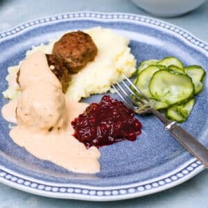 Dish on blueplatter with meatballs, gravy, mash, lingonberry jam and pressed cucumber.