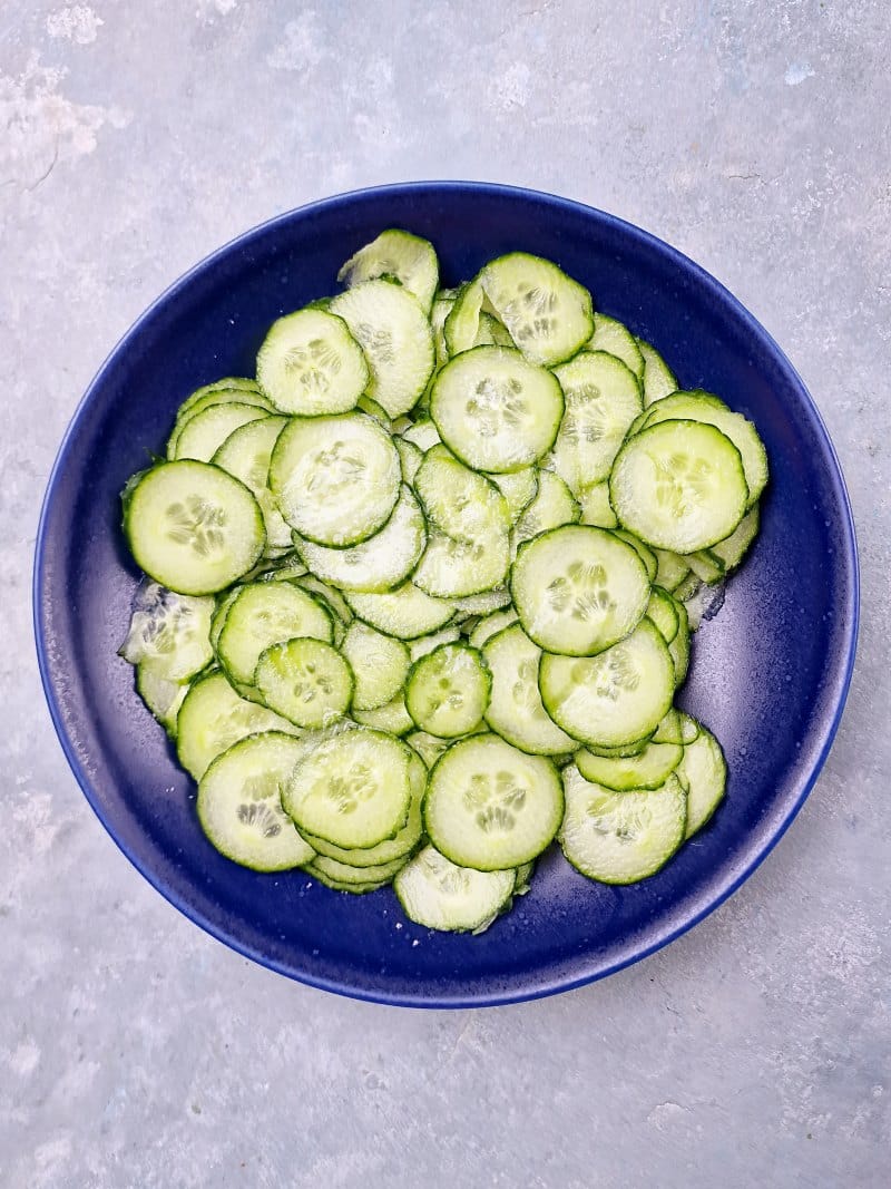 sliced cucumber on blue plate topped with salt. 