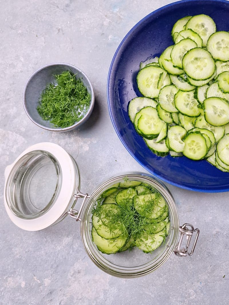 cucumbers in plate, dill in bowl and half full glass jar with layered cucumber slices. 