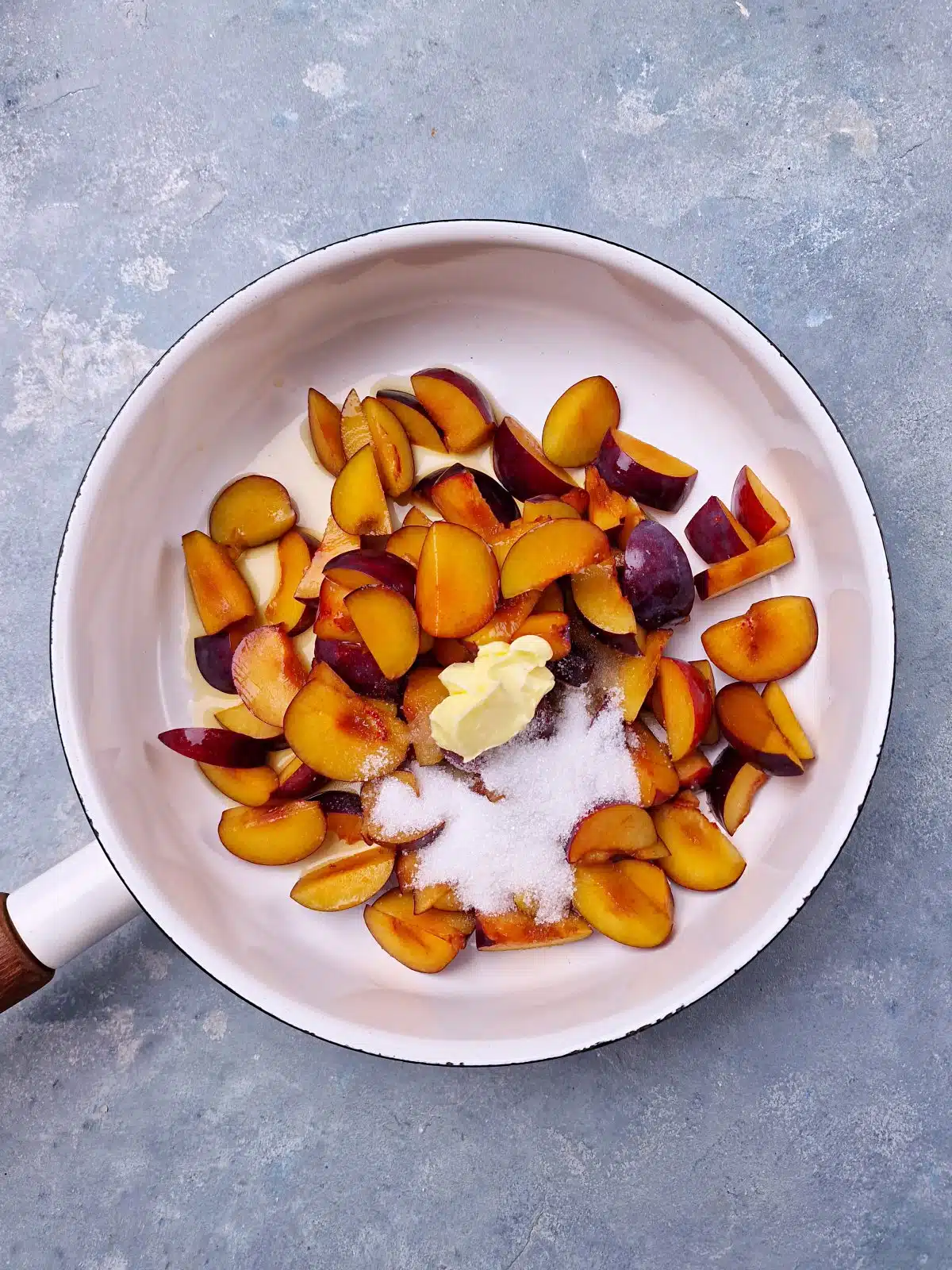 Plum slices on white pan with some sugar and butter on top. 