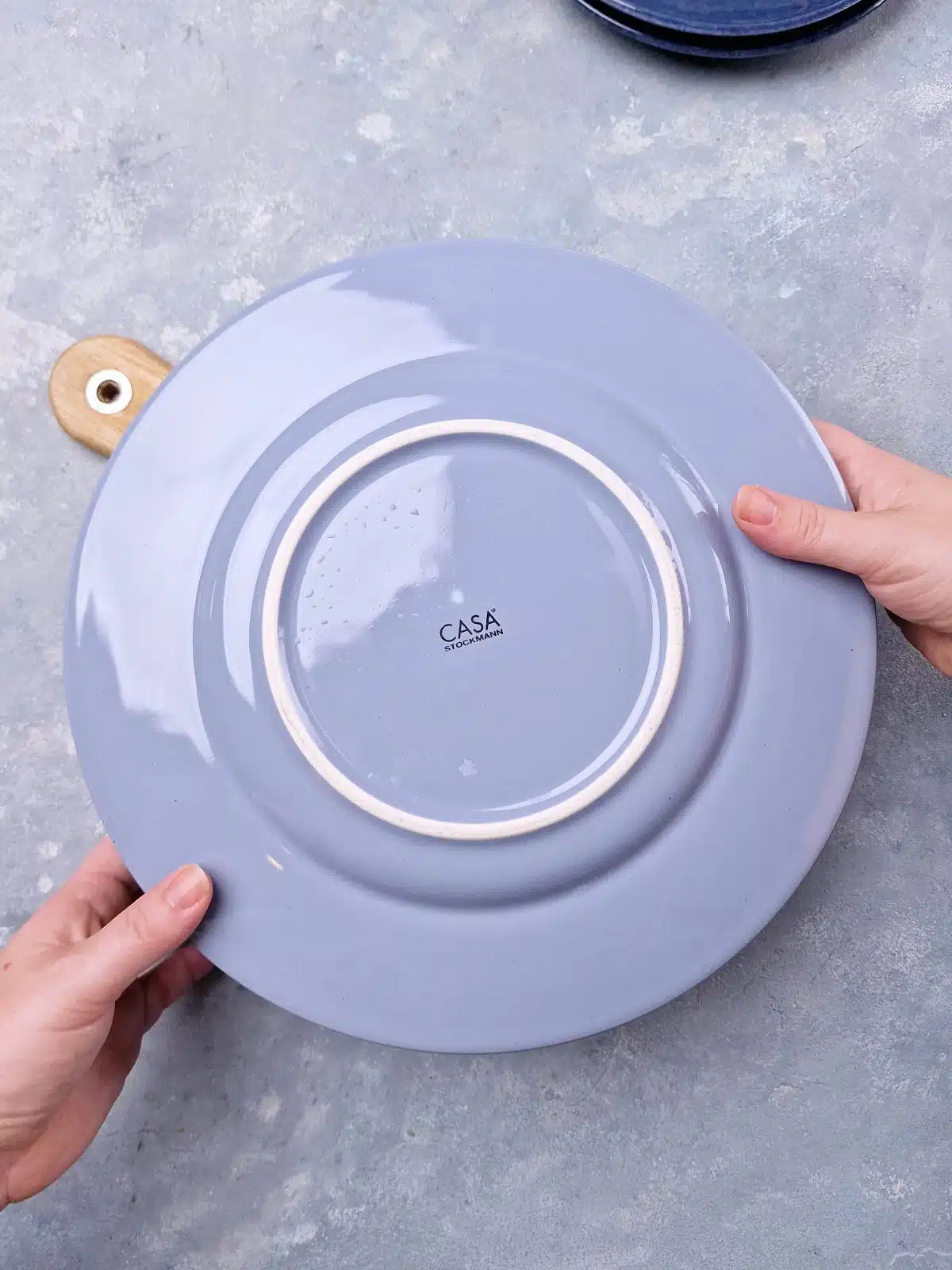 Blue plate covering the springform pan and hands lifting it to flip. 
