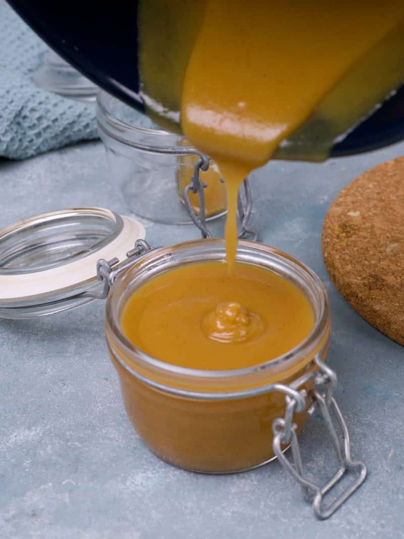 Mustard being poured in glass jar. 