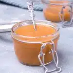 Mustard in two jars with spoon on blue background.