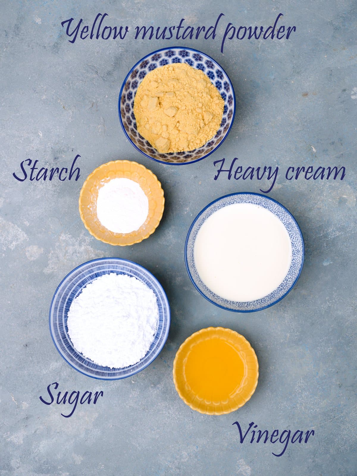 Ingredients for mustard laid on surface with labels; heavy cream, yellow mustard powder, starch, sugar and vinegar. 