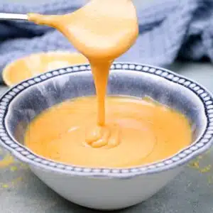 Yellow mustard in blue romantic bowl and spoon dripping the mustard and showing the consistency.