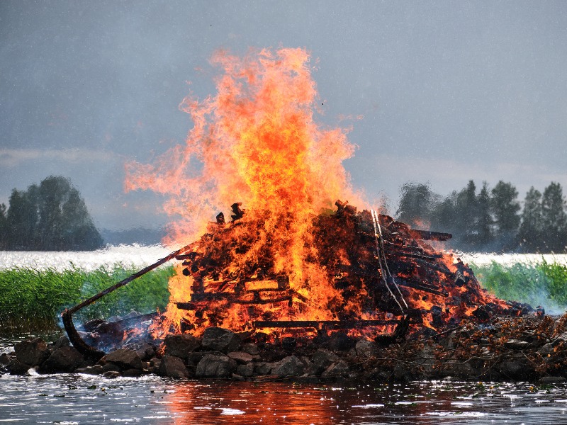 A large burning kokko; a pile of wood burning on coastal area. 