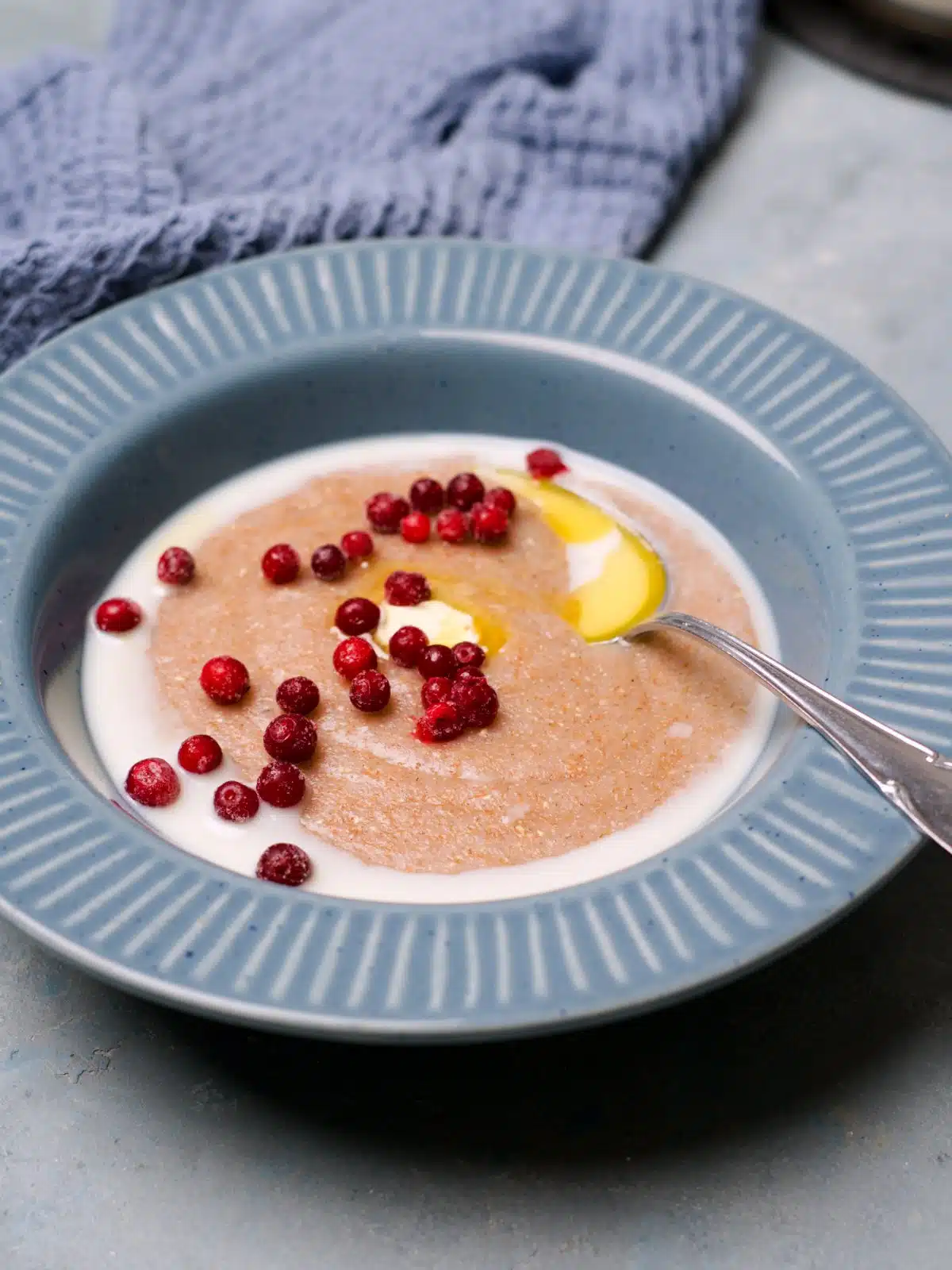 Velvety rye porridge on blue plate served with milk, butter and lingonberries.