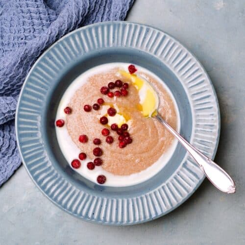 Porridge shot from above, rye porridge on blue plate with butterknob, milk and some frozen lingonberries