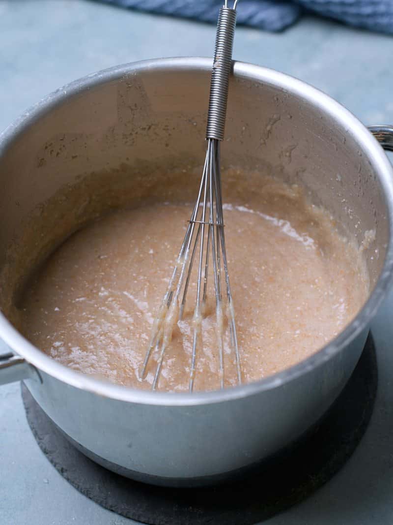 Thickened boiled brown porridge in pot with a whisk. 