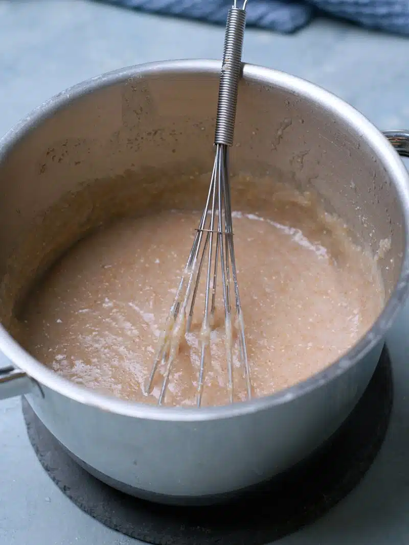 Thickened boiled brown porridge in pot with a whisk.