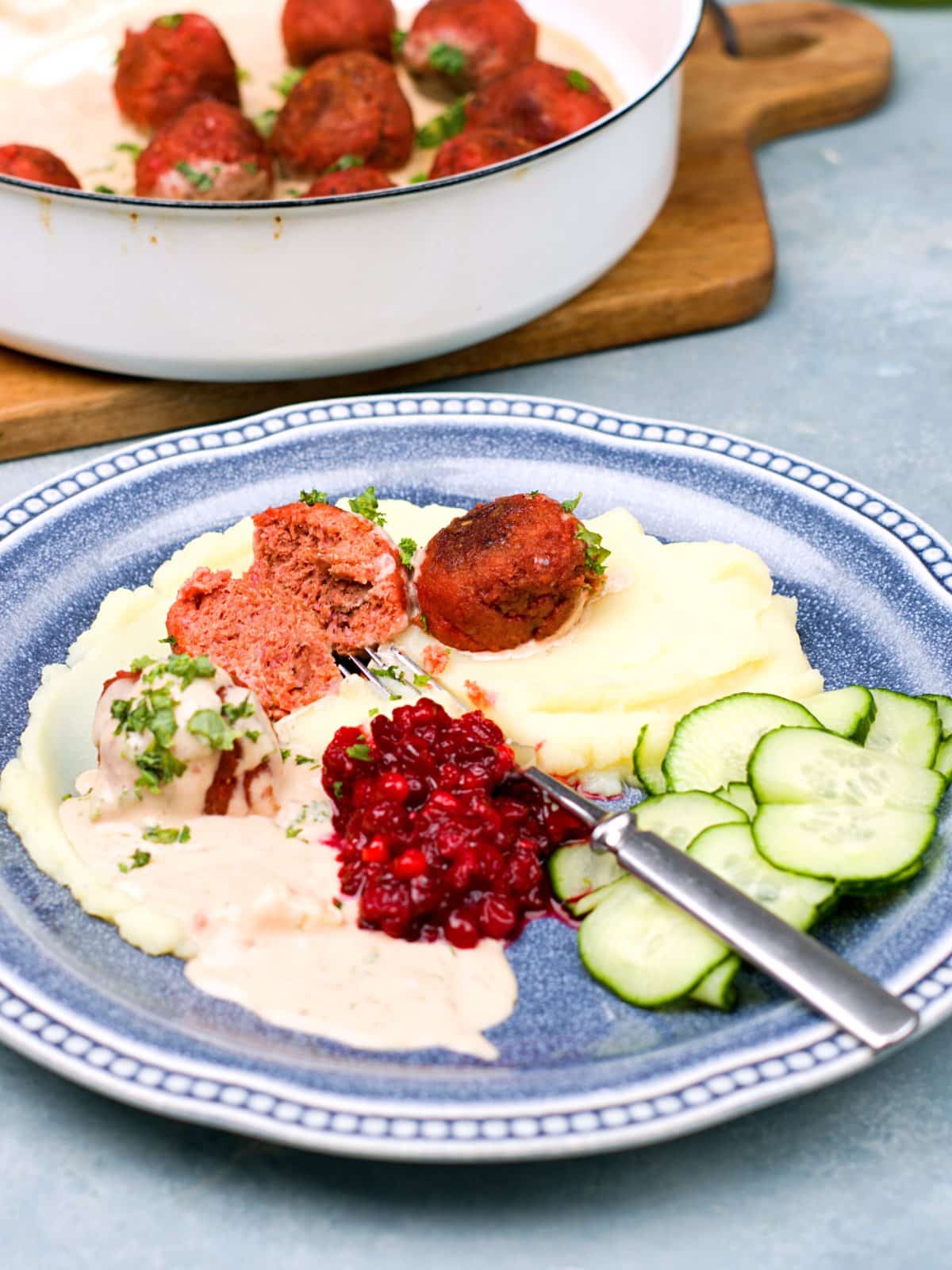 Closeup on a platter with meatballs, creamy sauce in soft potato mash. As condiments lingonberries and cucumber slices. 
