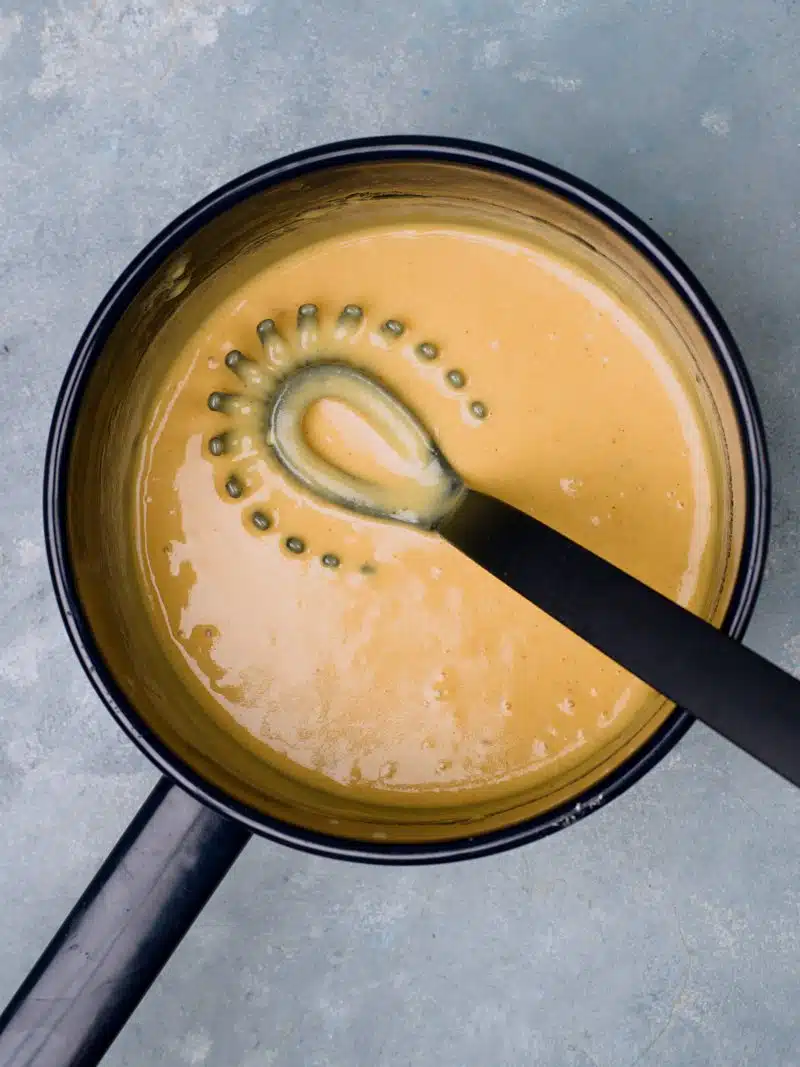 Boiled yellow sauce in bowl with a plastic whisk. 