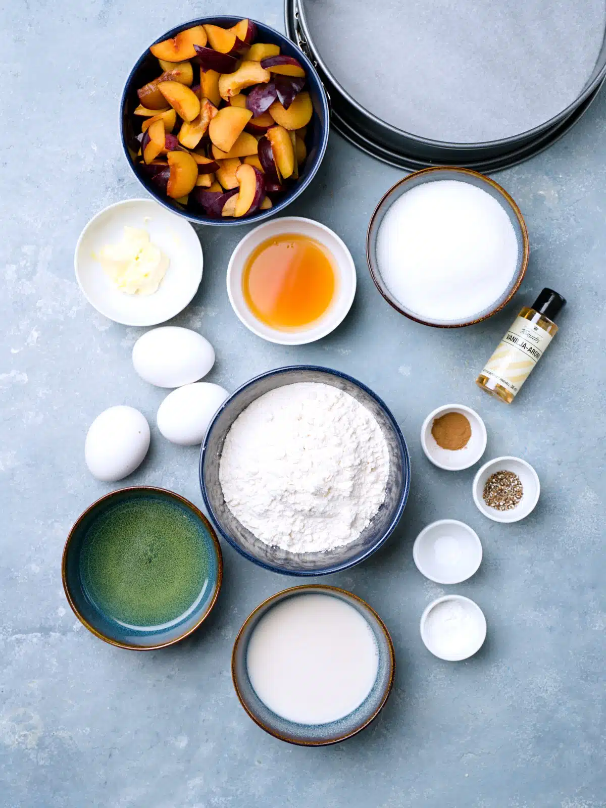 Ingredients for plum upside down cake on blue surface in cups.
