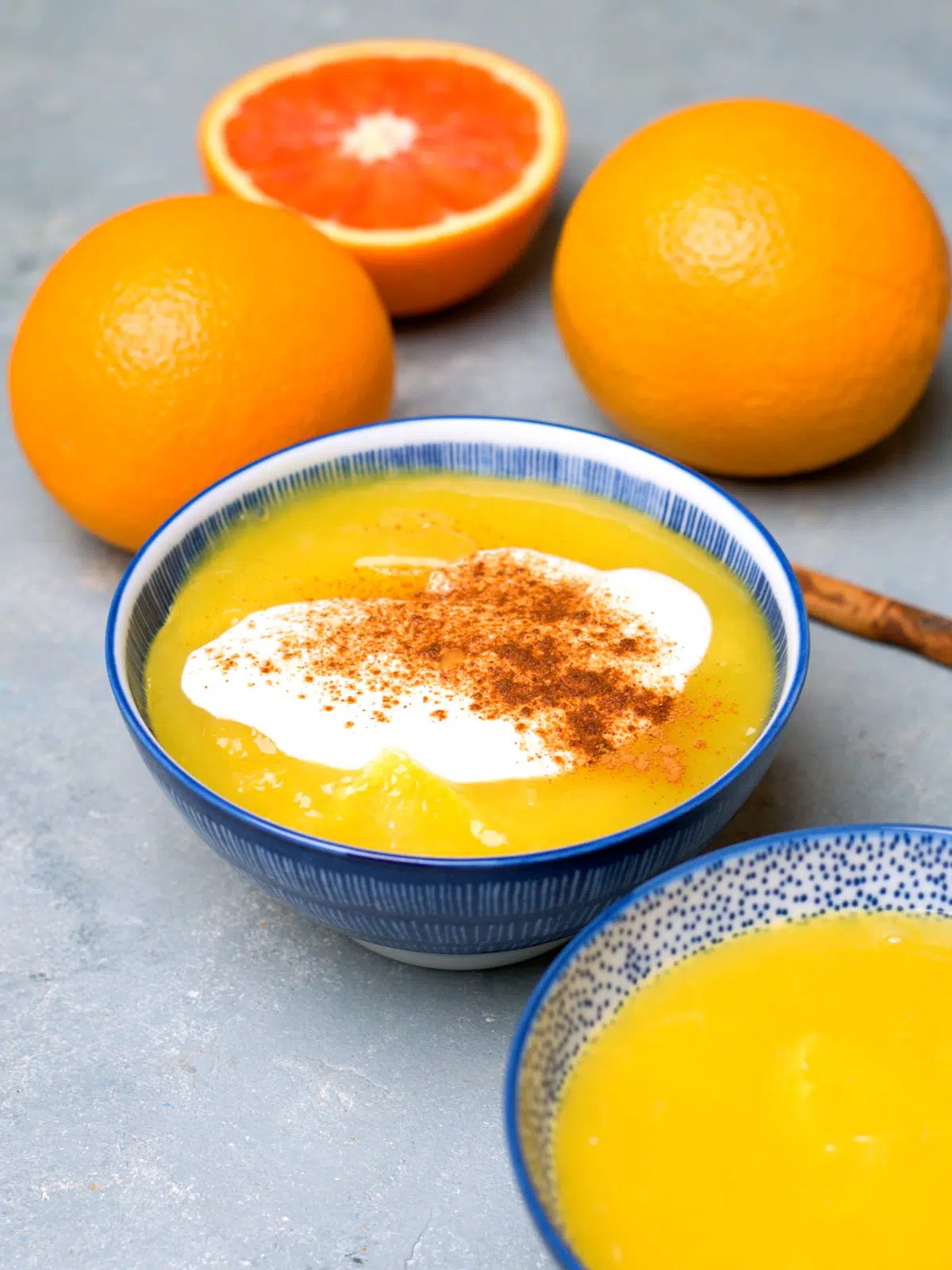 Orange sweet soup in blue bowls and oranges in the background. On top the kissel some whipped cream and cinnamon. 