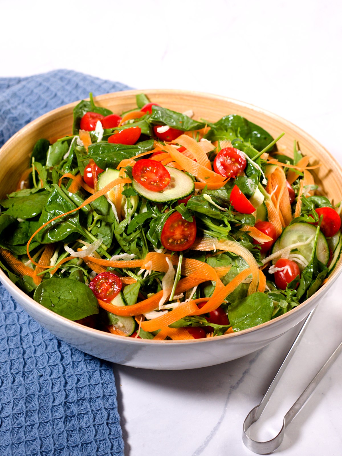 A large Ikea bowl filled with salad contianing greens, cucumberm cherry tomatoes and carrot strips and thinly sliced cabbage. 